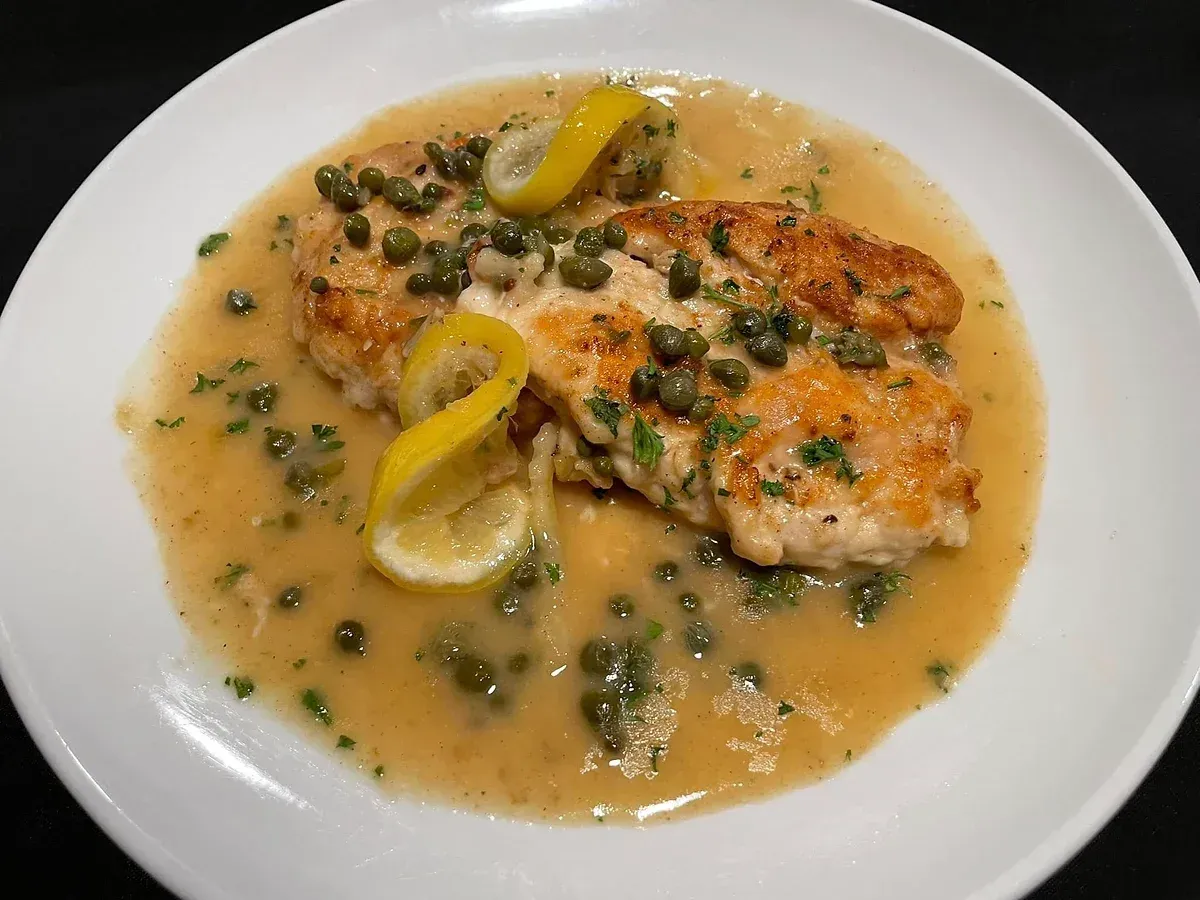 A white plate topped with chicken and sauce with lemon slices