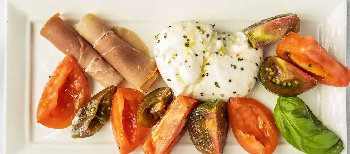 A white plate topped with tomatoes , mozzarella , basil and ham.