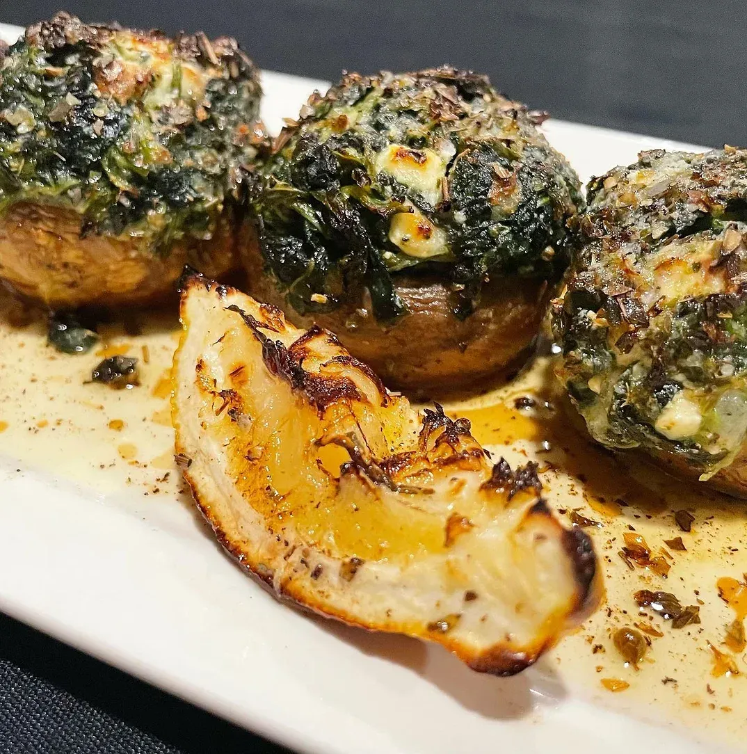 A white plate topped with stuffed mushrooms and spinach