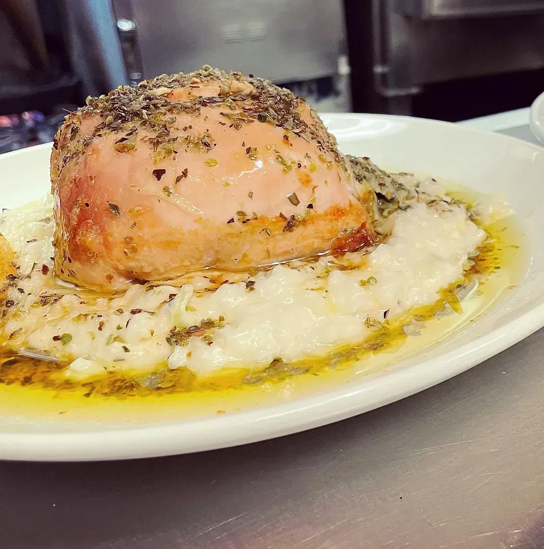 A white plate topped with a piece of meat and mashed potatoes