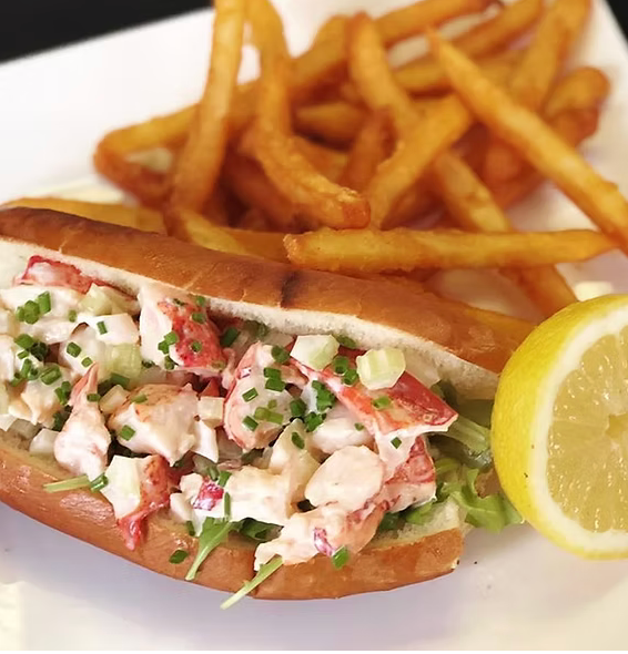 A lobster roll with french fries and a lemon wedge