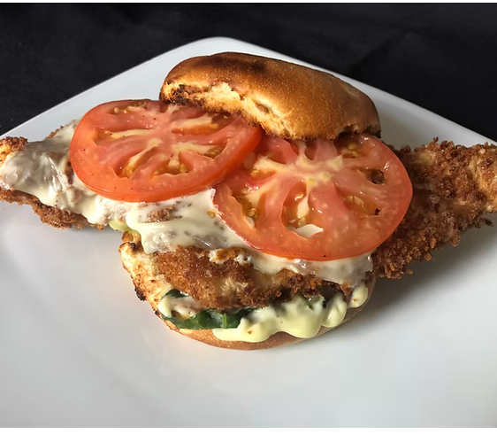A chicken sandwich with tomatoes and cheese on a white plate