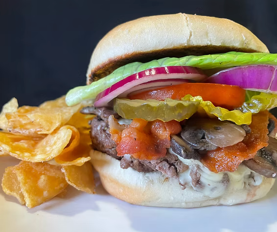 A close up of a hamburger on a bun next to potato chips