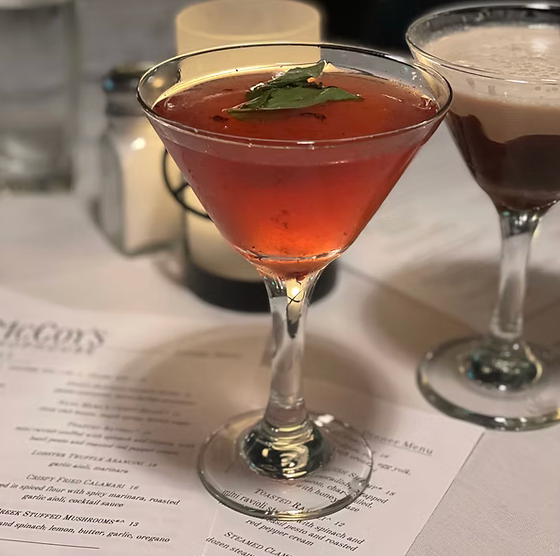 Two martini glasses are on a table next to a menu