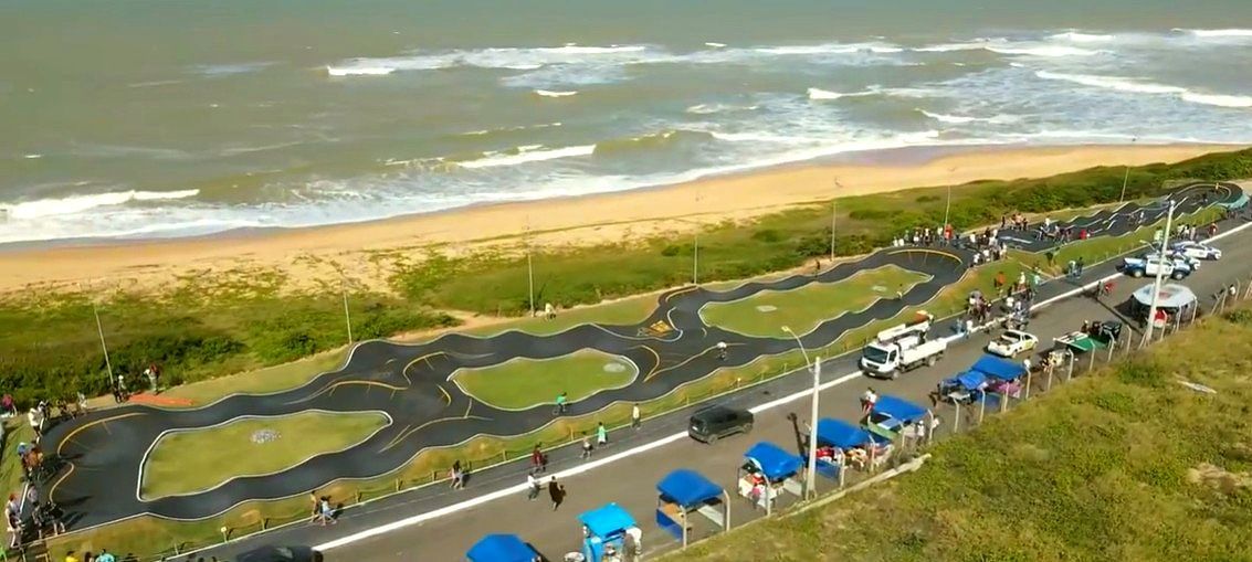 Pista de kart costeira ao lado de uma praia, com guarda-sóis azuis e ondas do oceano ao fundo.