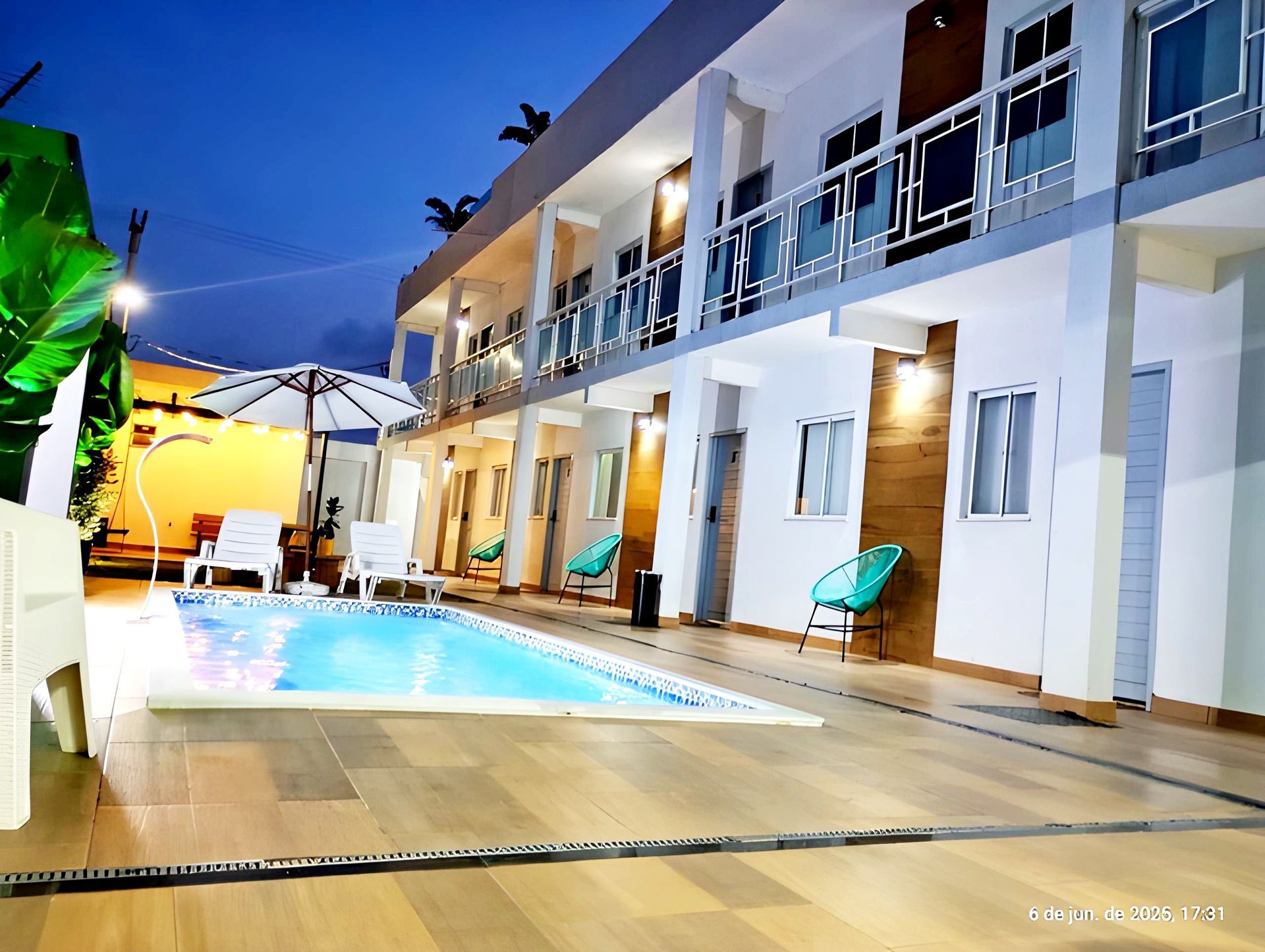 Pátio externo do hotel com piscina iluminada, espreguiçadeiras e varandas ao entardecer.