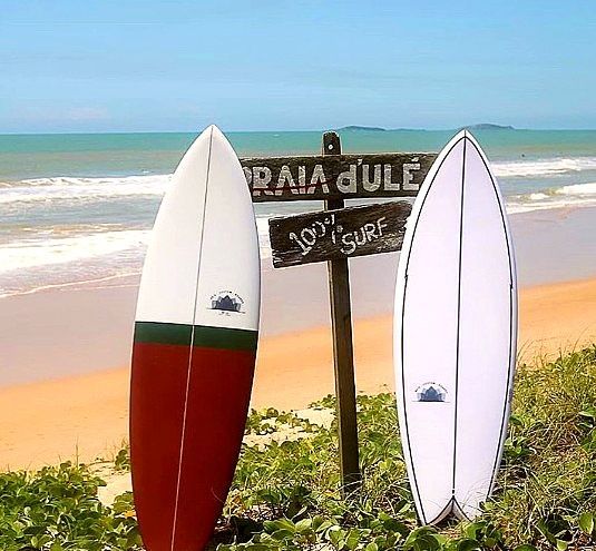 Duas pranchas de surfe ao lado de uma placa de praia em uma ensolarada costa tropical.