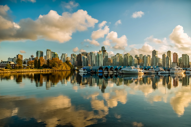 A city skyline is reflected in the water of a lake.