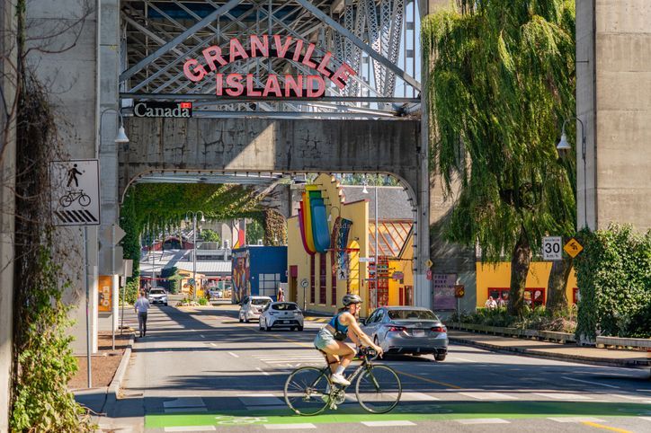 A man is riding a bike down a street under a bridge.