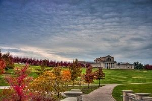 Park landscape with a building in the distance, a pathway, and colorful autumn trees under a cloudy sky.