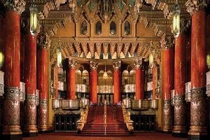 Ornate theater interior with red columns, staircase, and decorative ceiling.