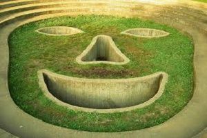 A large, grass-covered sculpture of a smiling face with concrete features in an outdoor setting.