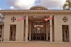 Beige building with central entrance, columns, flags, and round windows.