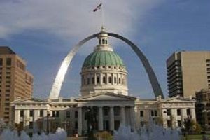 St. Louis Arch arches over the Old Courthouse building with a fountain in the foreground and city buildings.
