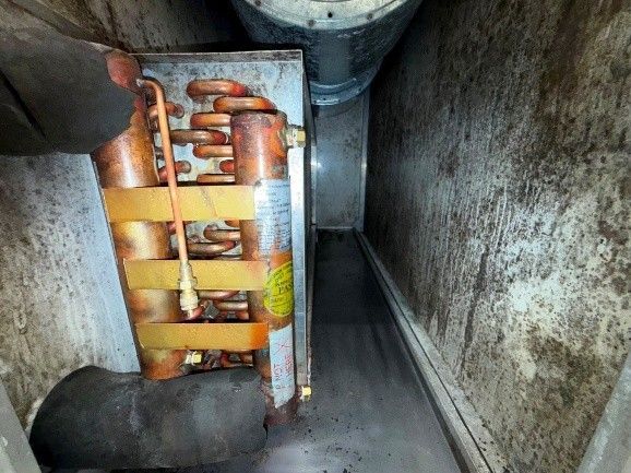 HVAC coil inside a dirty enclosure; a hand holding the coil. The coil is copper-colored.