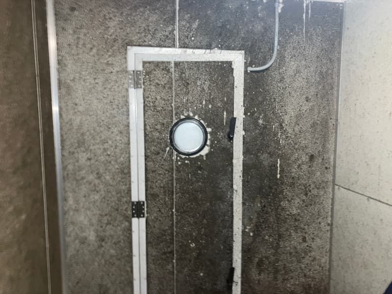Door with porthole window, surrounded by mold and grime on gray walls.