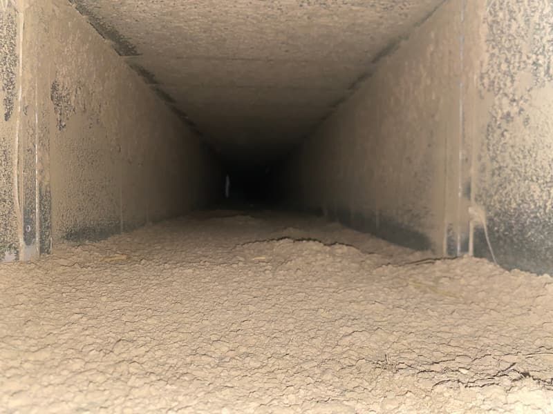 Inside of a rectangular air duct, coated in a thick layer of dust.