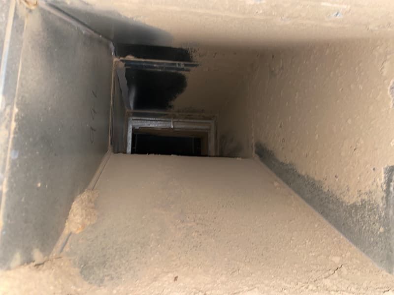 Dusty, rectangular air duct interior with a dark, obscured space at the end.