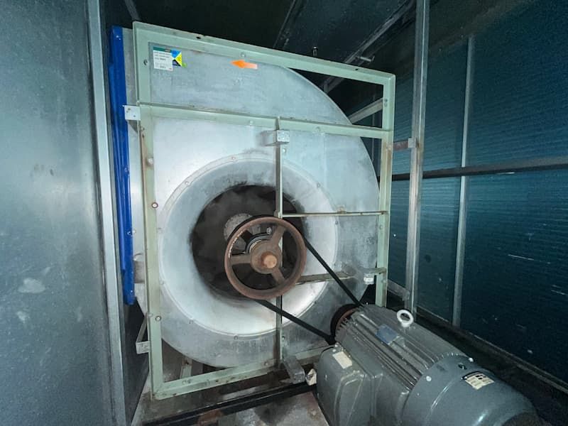 Large industrial fan with belt and motor, mounted in a metal enclosure.
