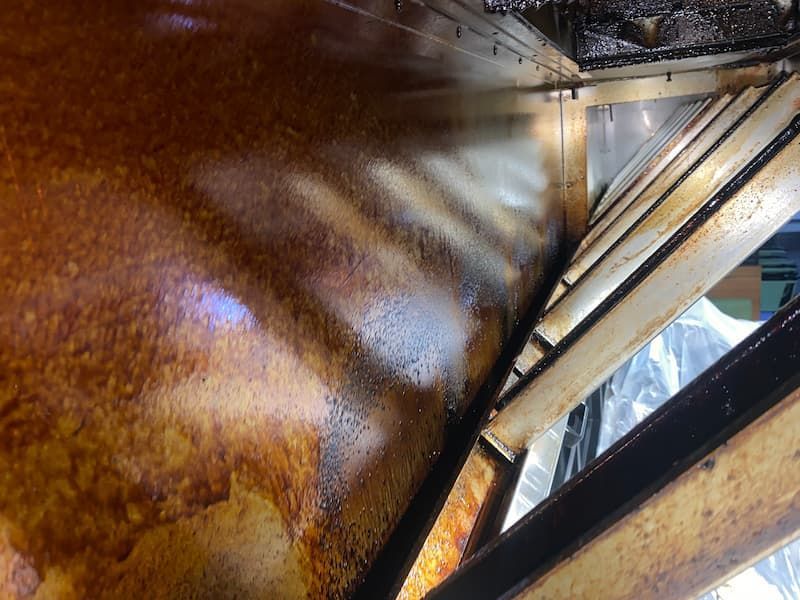 Greasy commercial kitchen exhaust hood interior. Brown residue coats the metal surfaces and baffle filters.