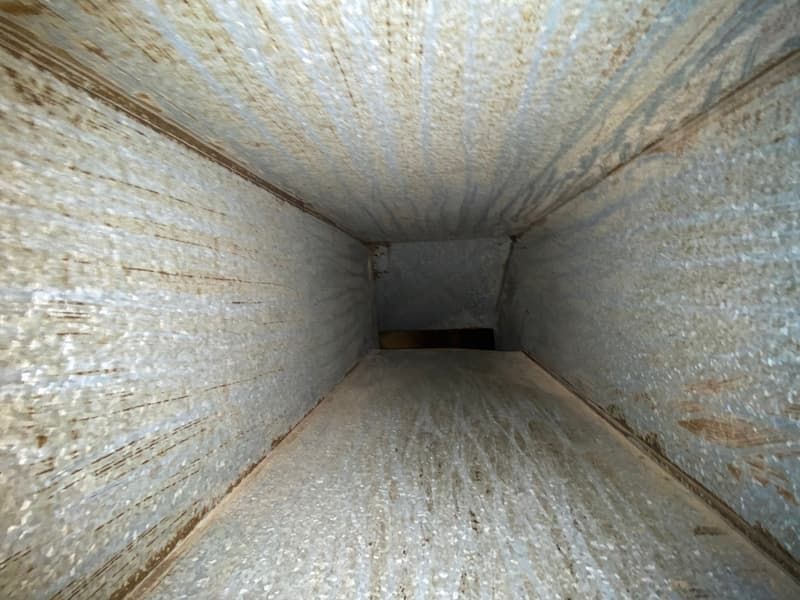 Inside view of a rectangular, metal air duct, showing dirt and debris buildup.