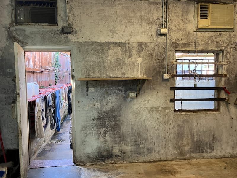Concrete room with open doorway leading to a laundry area with hanging clothes; window with bars.