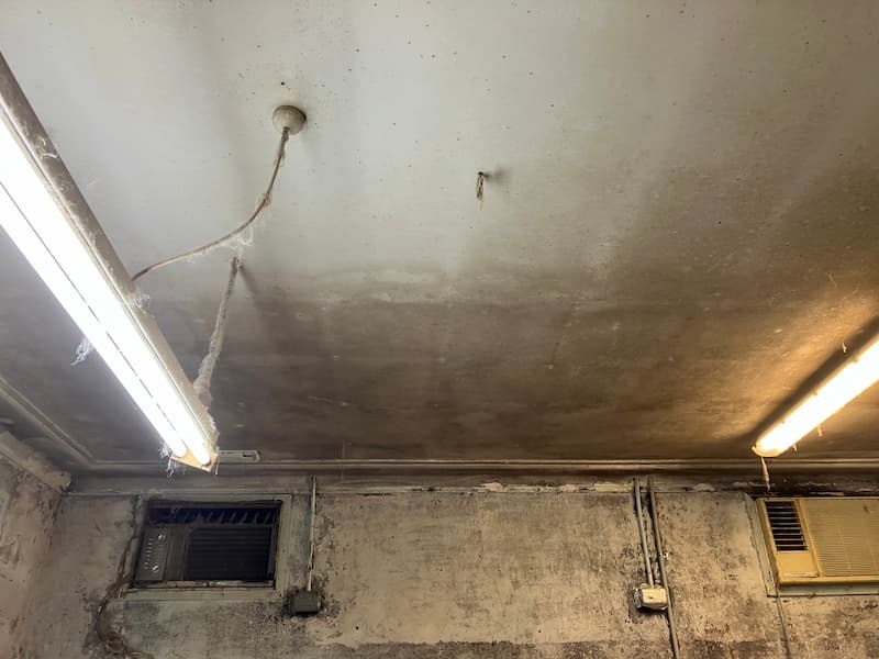 Ceiling and wall in a damp, aged space. Two fluorescent lights, a vent, and an AC unit are visible.