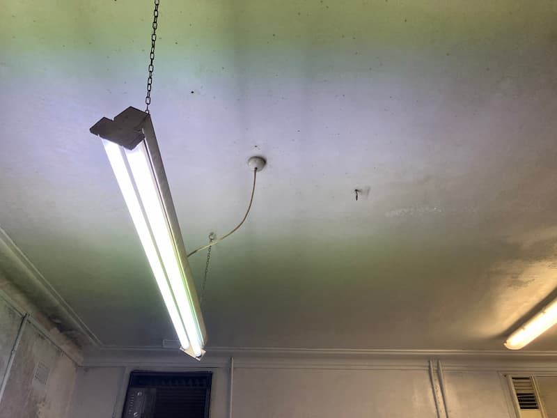 Fluorescent ceiling light hanging from a chain, illuminating a white ceiling.