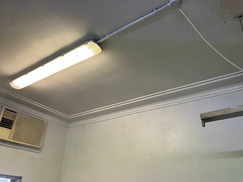 Fluorescent light fixture on a gray ceiling, above white walls, with an air conditioner unit.