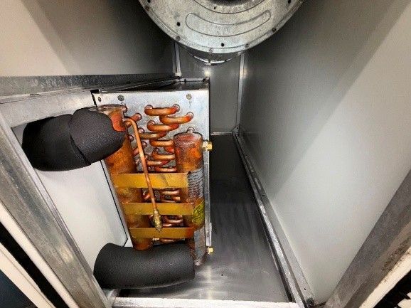 Interior view of an air conditioning unit; orange and copper coils, black insulated pipes, and a silver enclosure.