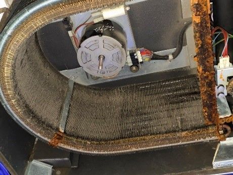 Close-up of a corroded HVAC evaporator coil, motor, and related components, showing rust and wear.