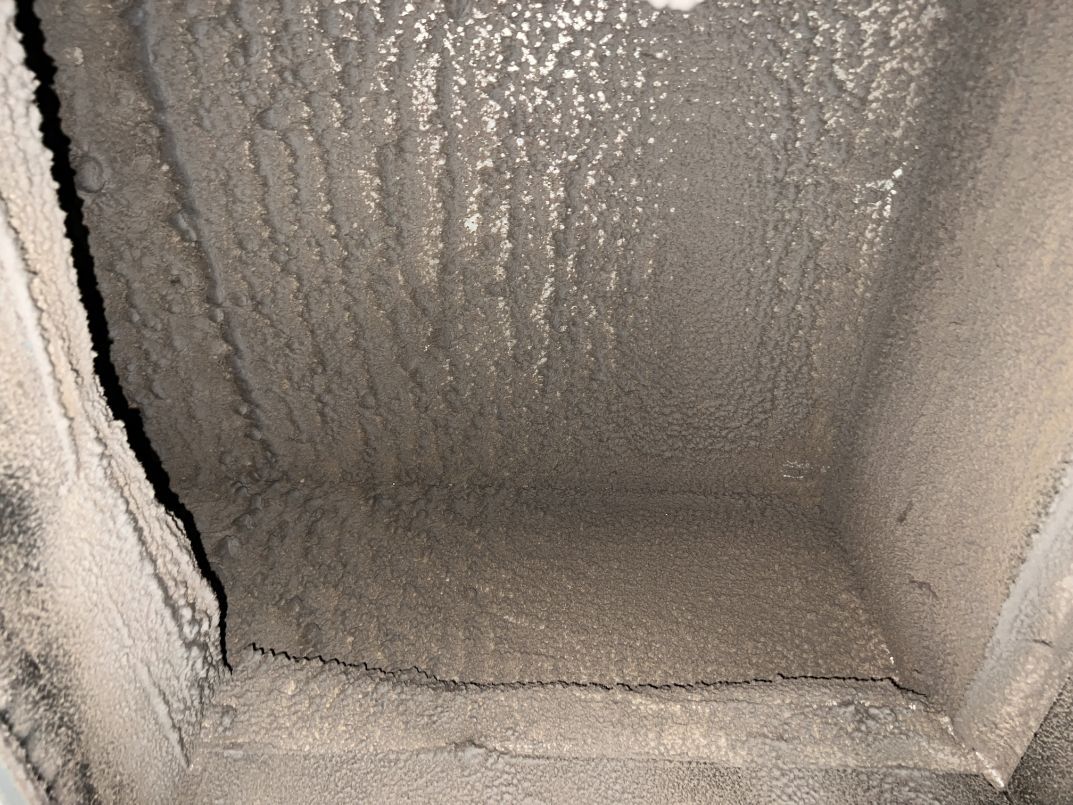 Interior view of a dusty air duct. Thick layer of grime covers the surfaces.