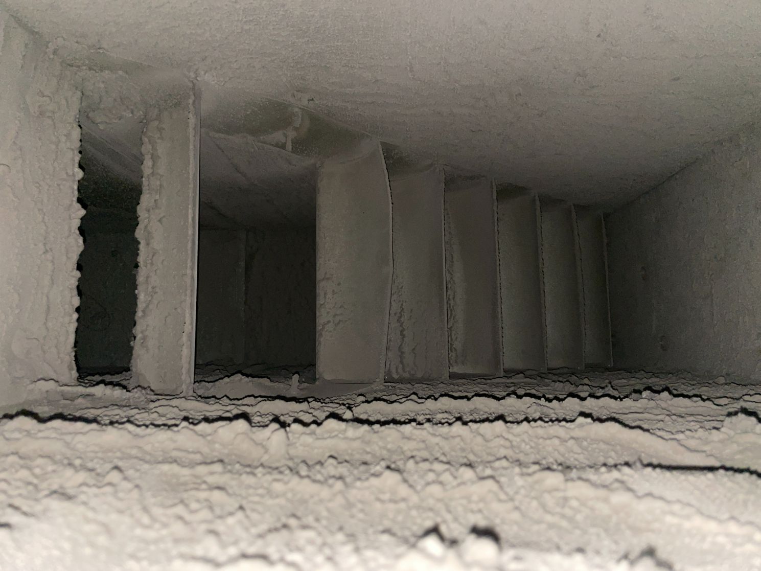Interior view of a dusty air duct with vertical supports covered in a thick layer of debris.
