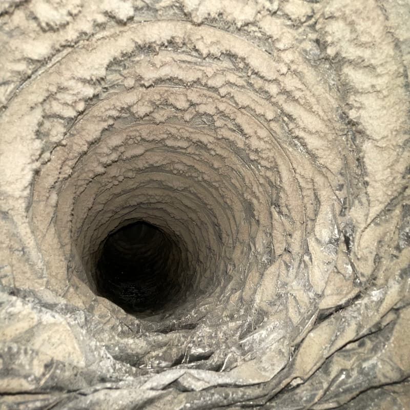 Dirty air duct, interior view. Thick coating of dust and debris inside a dark, circular passage.
