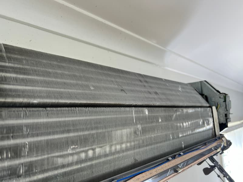 Indoor AC unit, open. Metal fins visible, dusty. Mounted on white wall below a ledge.