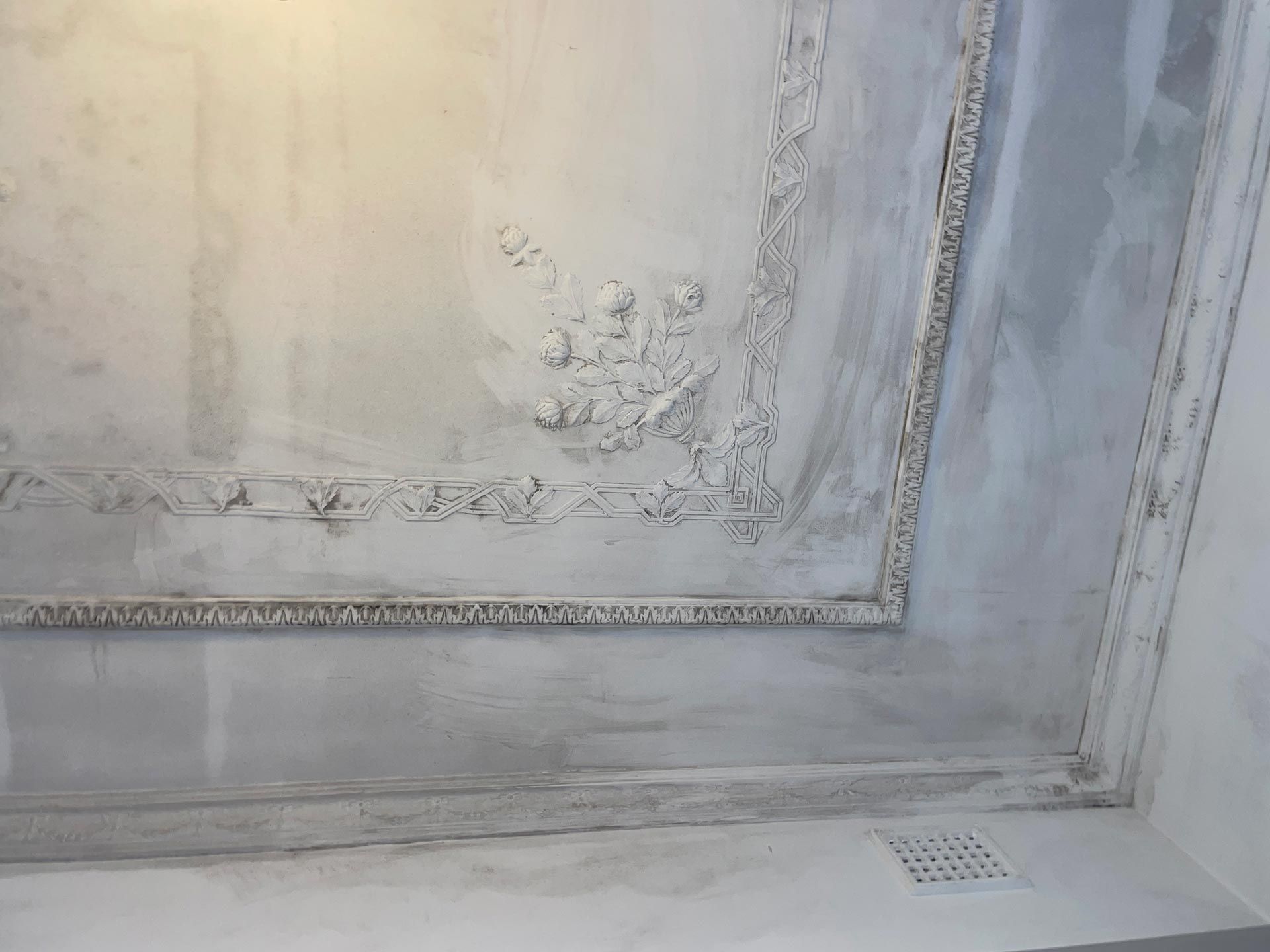 Gray and white ceiling with decorative molding and ventilation grate.