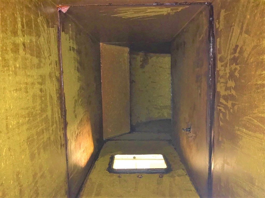 Inside of a yellow-painted rectangular metal duct, with a rectangular obstruction in the middle.