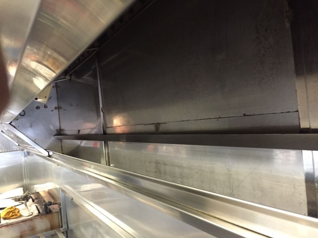 Inside view of a stainless steel commercial kitchen hood with a shelf and visible seams.