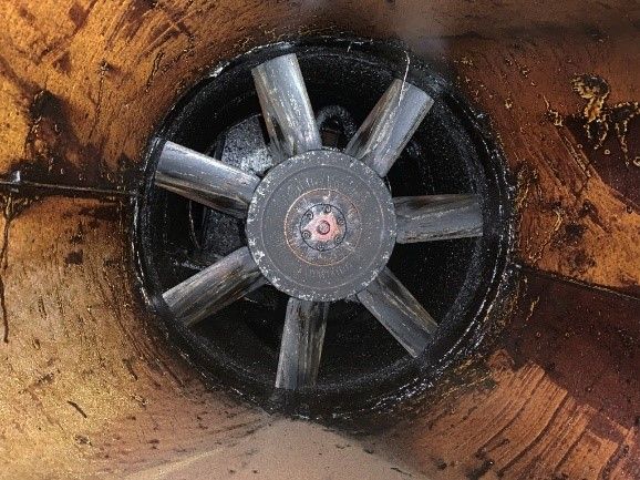 An inside view of a dark, cylindrical structure featuring a fan with eight blades coated in oil.
