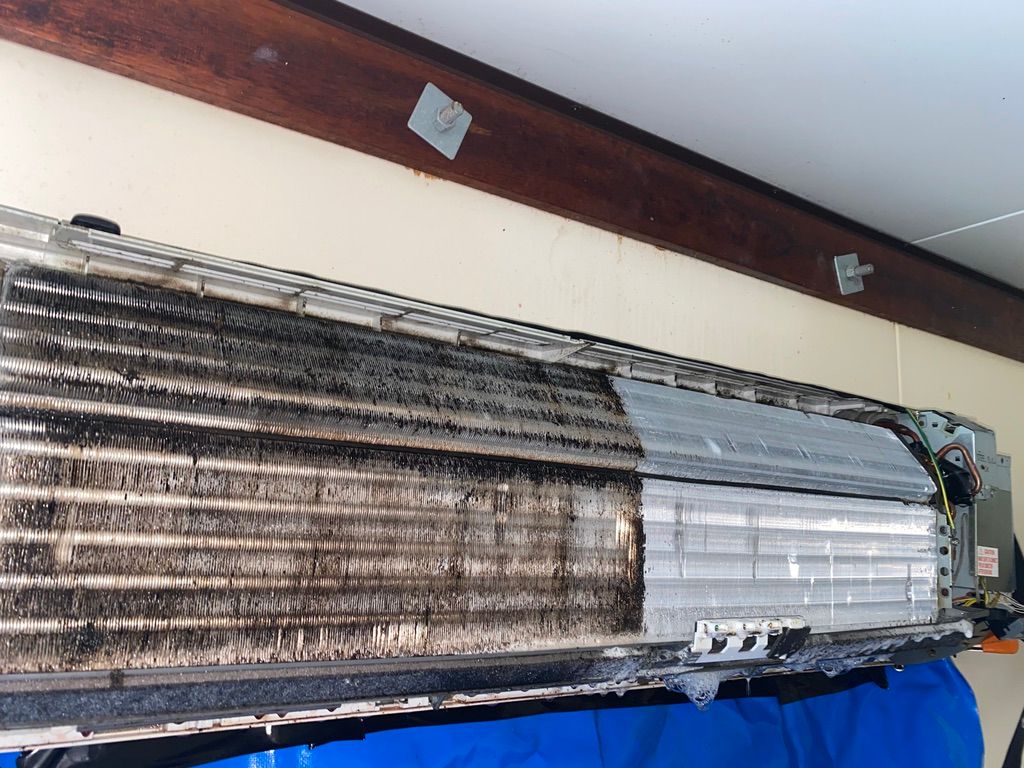 A dirty air conditioning unit being cleaned; half is clean, the other half is caked in black grime.