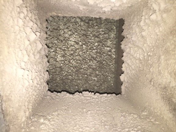 Inside of a square air vent heavily coated with thick layers of dust and debris.