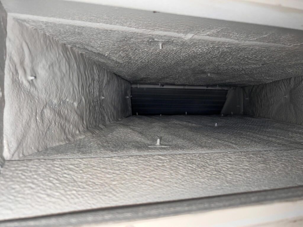 Inside of an air duct, coated in thick white dust and debris, with visible clips.