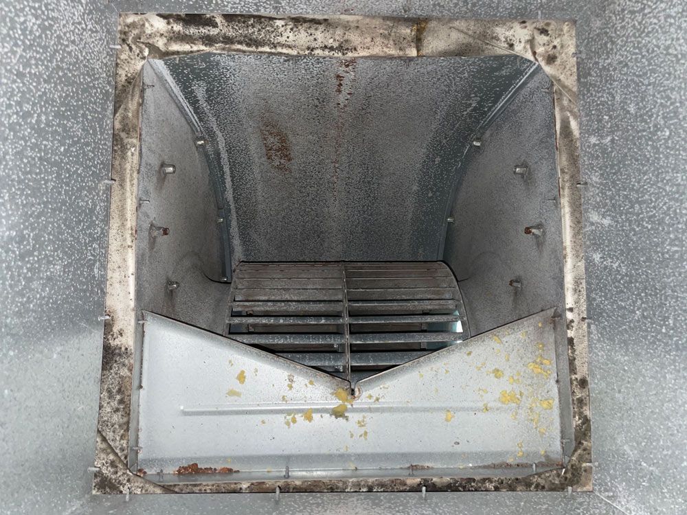 Metal air duct interior with a fan, showing dust and debris buildup.