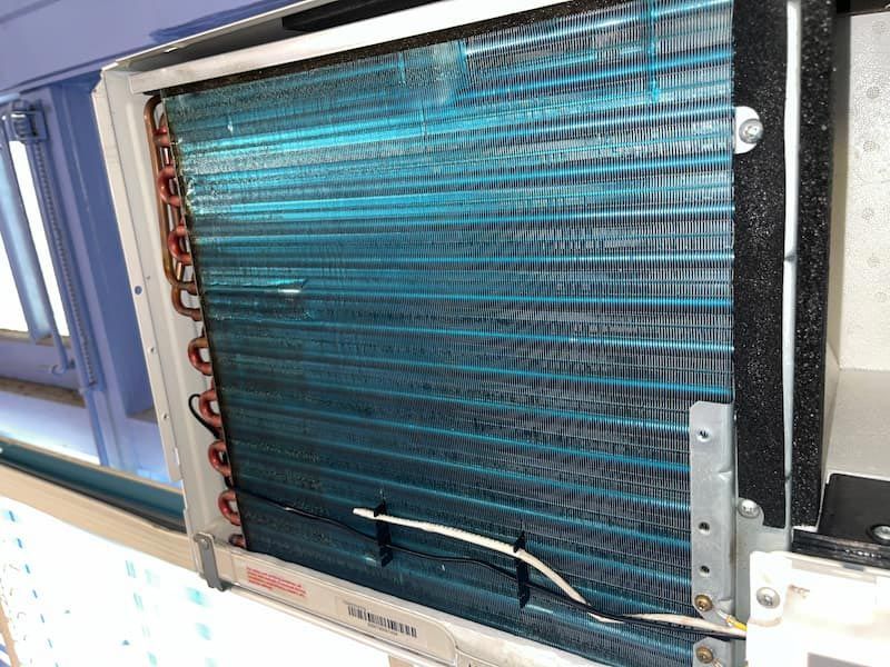 Indoor air conditioner unit with blue cooling fins and copper tubing.