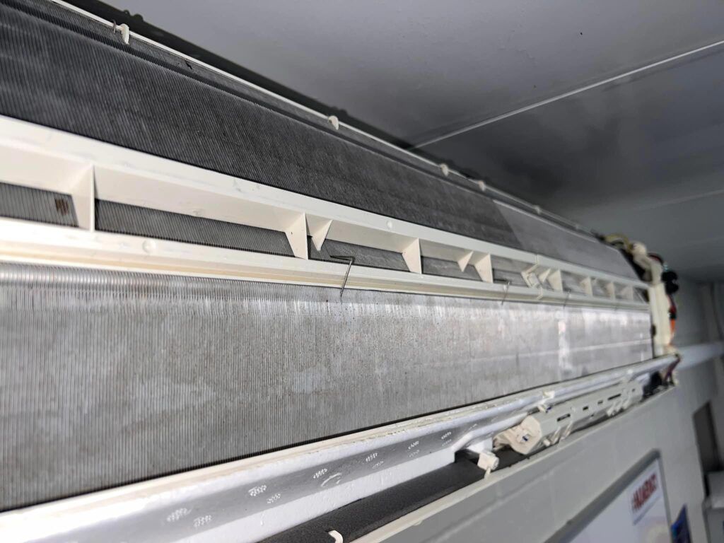 Close-up of a dirty, opened air conditioning unit, showing the internal cooling fins.