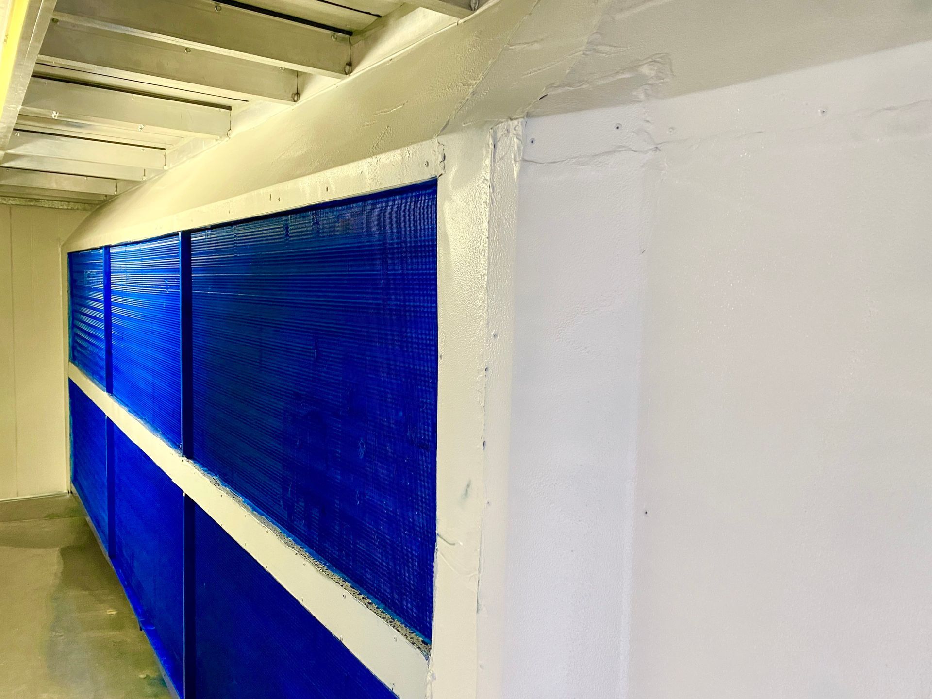 Blue cooling pads within a white building's wall, positioned under a white beam.