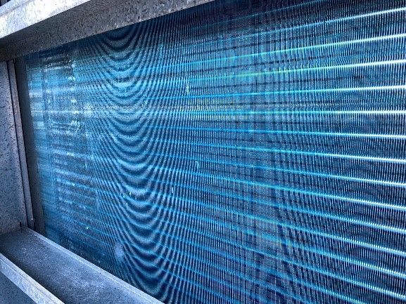 Close-up of a blue HVAC evaporator coil, with parallel fins and a metal frame.