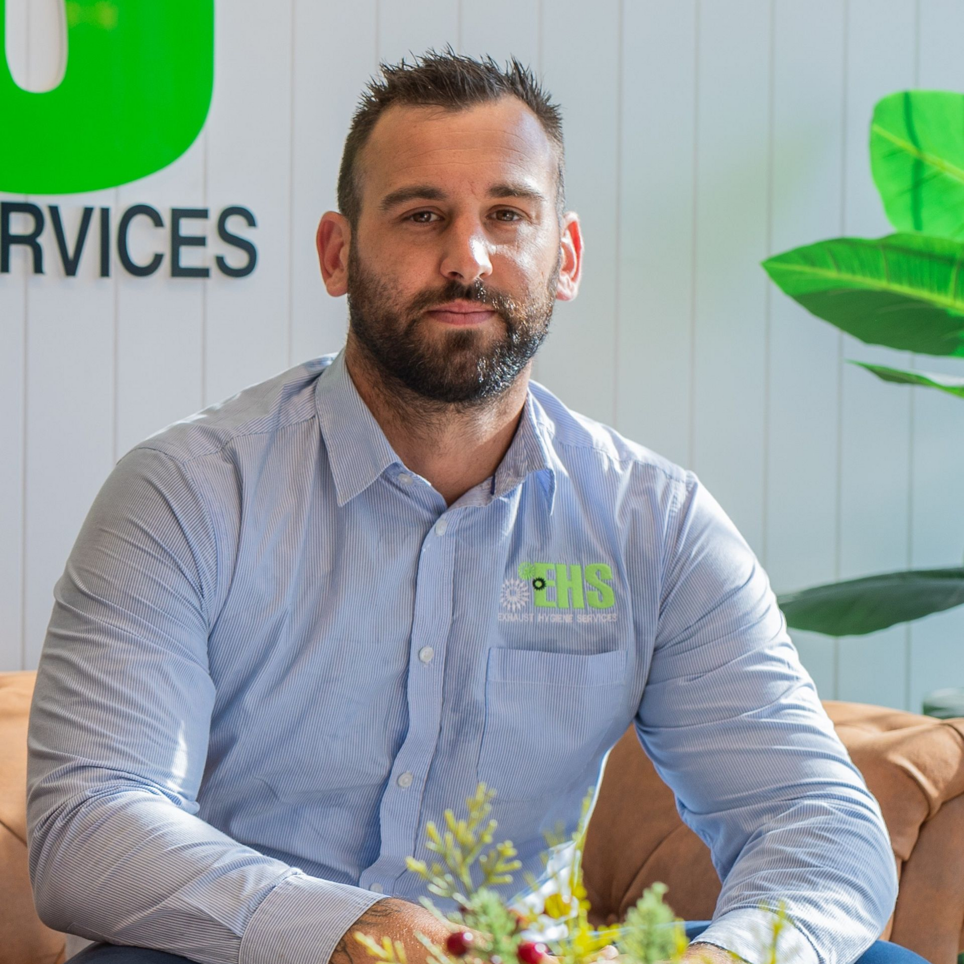 Man with a beard in a blue button-down shirt seated in a modern office with 