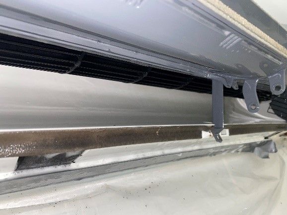 Inside view of an air conditioner showing vents, a metal bar, and plastic parts in white and gray.