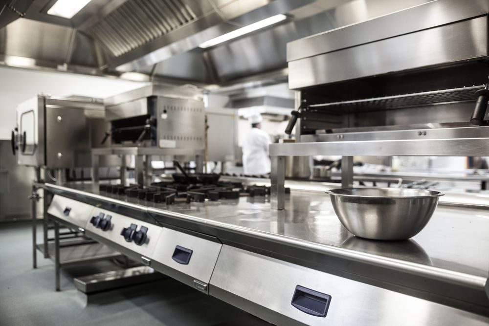 Stainless steel commercial kitchen with stovetop, ventilation hood, and bowl.
